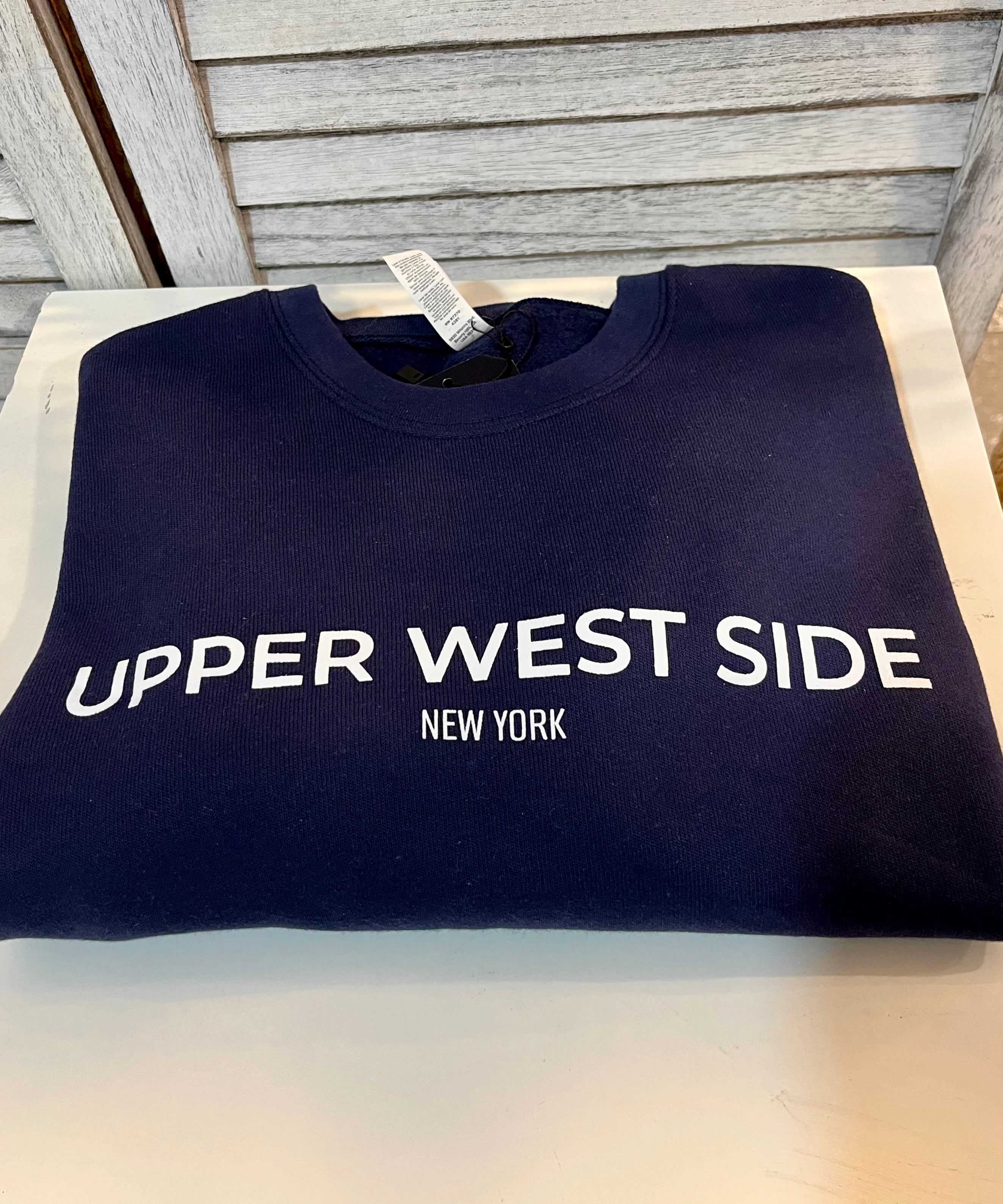 A navy blue crewneck sweatshirt with 'Upper West Side' text printed on the front